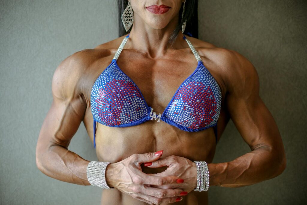 Strong female bodybuilder in blue rhinestone bikini showcasing muscular physique. Fitness and strength concept.