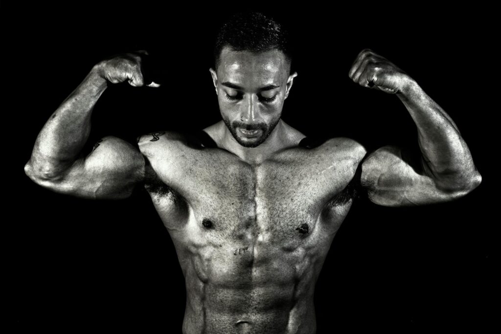 Black and white photo of a muscular male bodybuilder flexing his biceps in a dramatic pose.