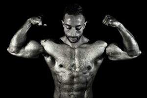 Black and white photo of a muscular male bodybuilder flexing his biceps in a dramatic pose.