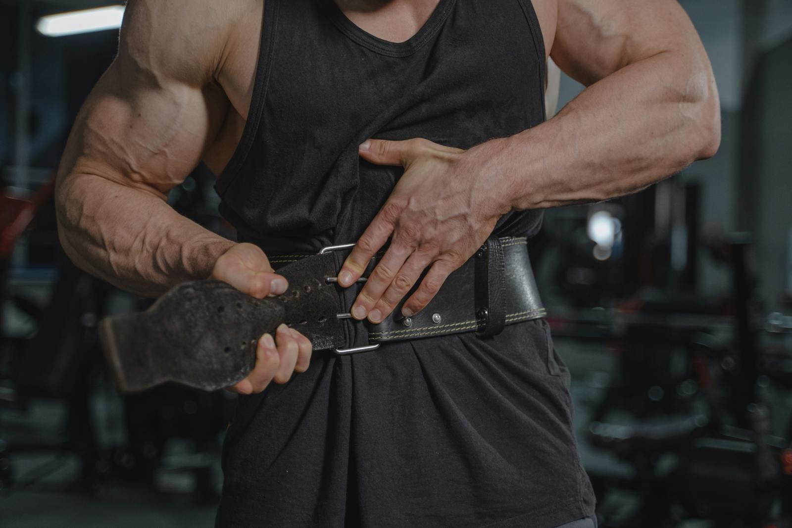 Close-up of a muscular man adjusting a weightlifting belt in a gym setting.